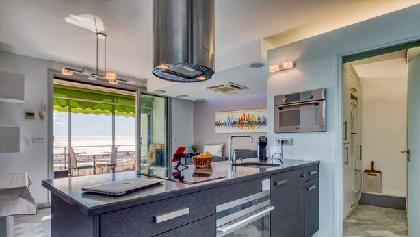 A modern kitchen with a large island, stainless steel appliances, and a view through the window. - The Splendid Grande Pyramide with Sea View, Wi-Fi, and Air Conditioning (La Grande-Motte)