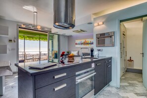 A modern kitchen with a large island, stainless steel appliances, and a view through the window. - The Splendid Grande Pyramide with Sea View, Wi-Fi, and Air Conditioning (La Grande-Motte)