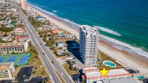 Luchtbeeld van een kustgebied met een opvallend hotel, een strand en een weg.