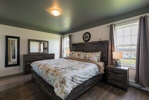 A bedroom with a bed, a dresser, a nightstand, a window with curtains, and a wall clock. - Morrison’s Beach Road Island Retreat (Georgetown)