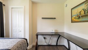 A hotel room with a bed, a desk with a computer, a painting on the wall, and a door.