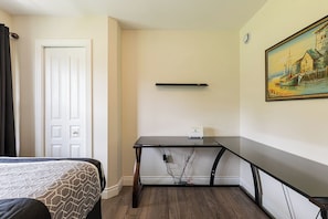 A hotel room with a bed, a desk with a computer, a painting on the wall, and a door.