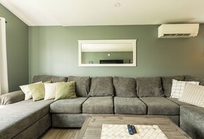 Ein Wohnzimmer mit Ecksofa, Couchtisch und einem Wand-Fernseher.