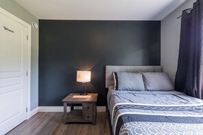 Ein Schlafzimmer mit Bett, Nachttisch, Lampe und einer Tür.