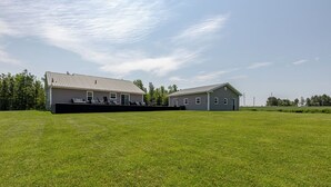 A large, open grassy field with two buildings, one with a covered porch and another with a garage.