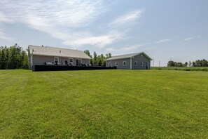 A large, open grassy field with two buildings, one with a covered porch and another with a garage.