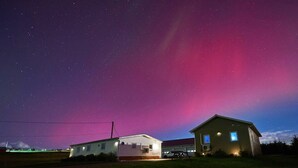 Ein ländliches Haus mit Garage und kleiner Werkstatt, unter einem sternenübersäten Nachthimmel mit Polarlichtern.