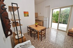 A compact kitchen with a dining table, a wooden chair, and a small shelf unit. - Villetta Macao 1 - 50 mt. dal mare 2 camere, clima (Torre Suda)