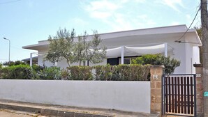 Un bâtiment moderne doté d’un toit plat, de murs extérieurs blancs et d’une entrée fermée par un portail.