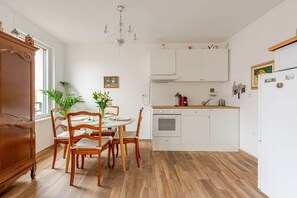 Een keuken met houten kastjes, een eettafel met stoelen, een kroonluchter en een koelkast.