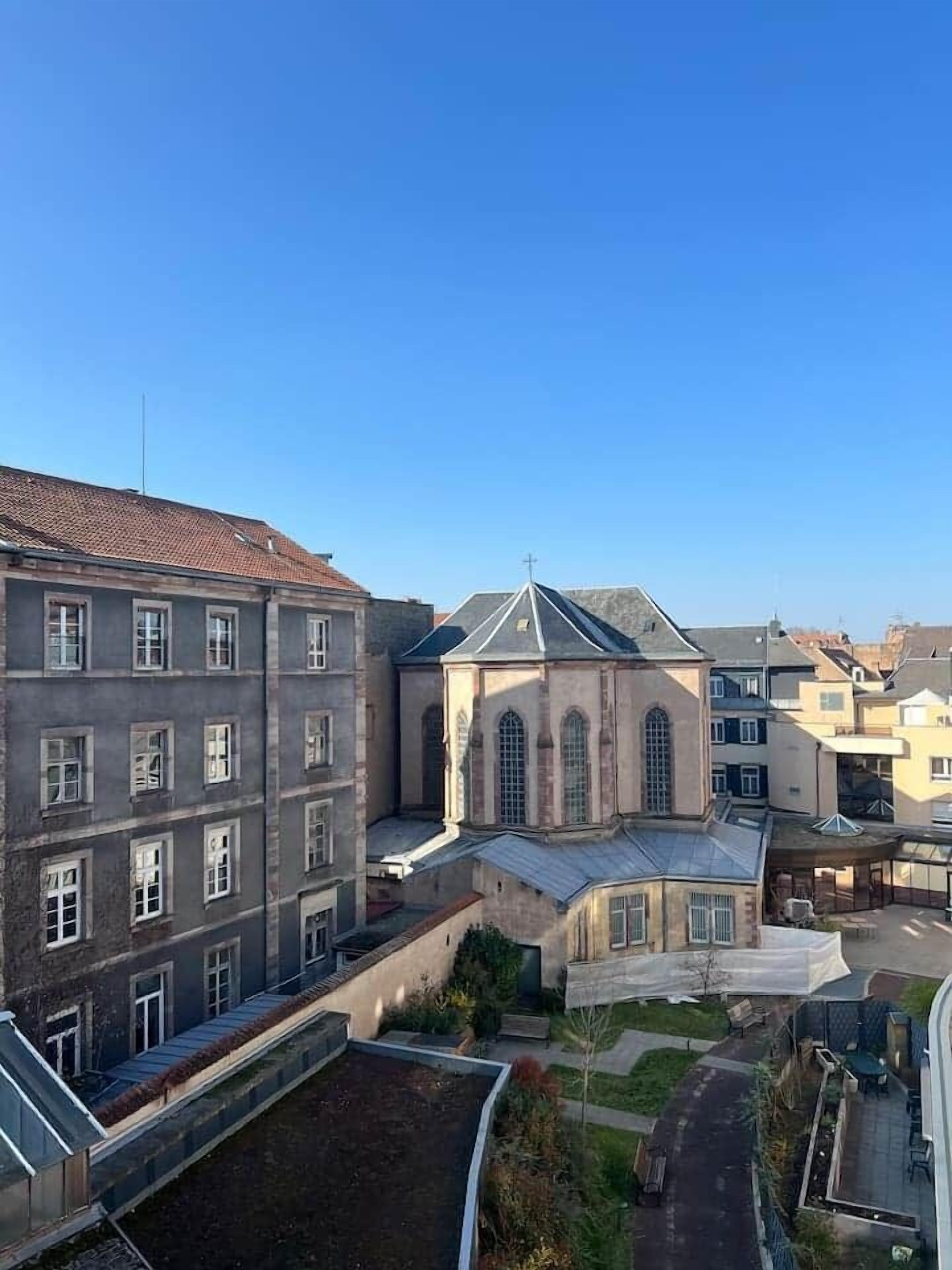 Un edificio a più piani con un cortile centrale, che include una chiesa con una croce in cima, circondata da edifici residenziali.