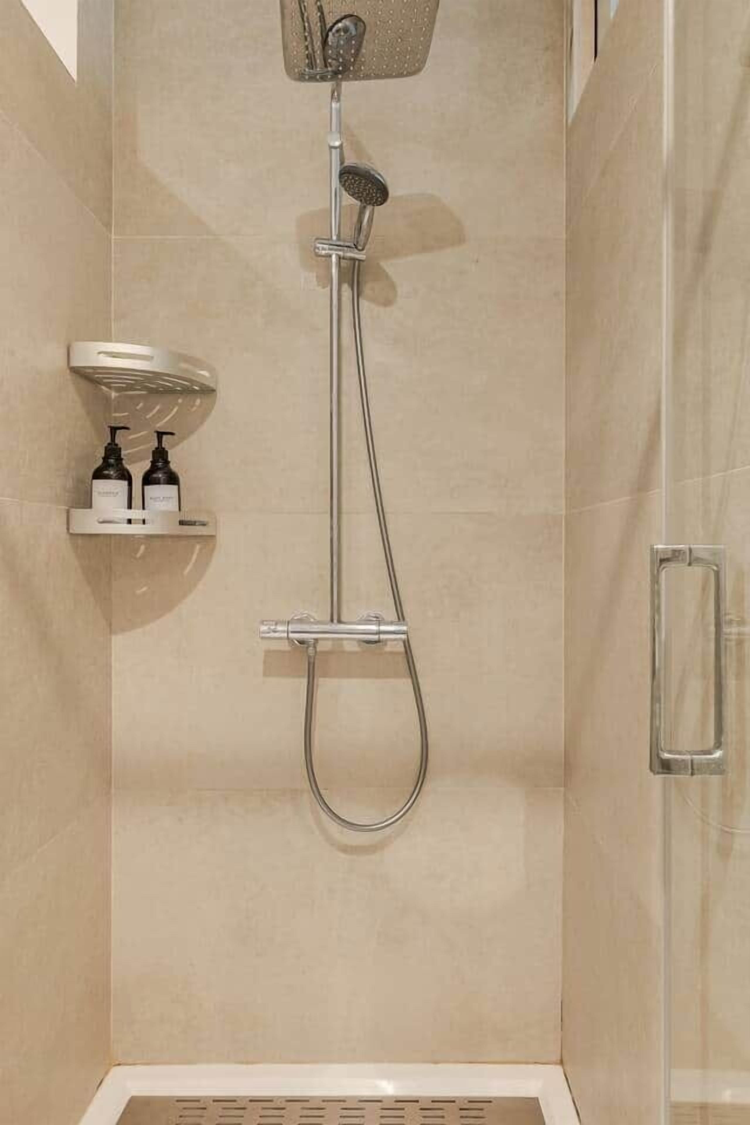 Una ducha con cabezal de ducha de mano, panel de control en la pared y zona de ducha con paredes de vidrio.