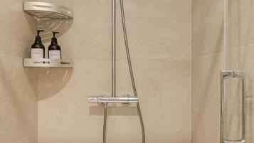 Una ducha con cabezal de ducha de mano, panel de control en la pared y zona de ducha con paredes de vidrio.