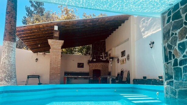 A swimming pool with a stone wall and a wooden pergola. - CASA CABERNET ideal location for building memories (Parras de la Fuente)