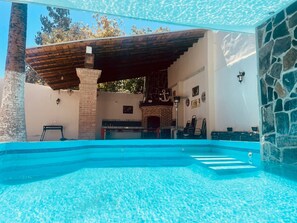Una piscina con una parete in pietra e un pergolato in legno.