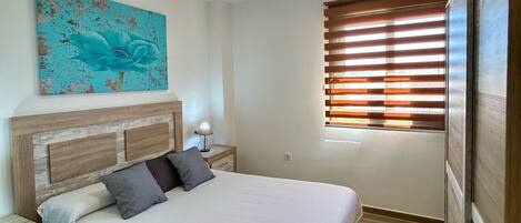 Un dormitorio con una cama, una mesita de noche, una lámpara, una ventana con persianas y una lámpara en el techo.