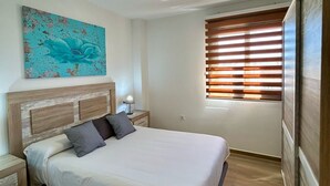 Un dormitorio con una cama, una mesita de noche, una lámpara, una ventana con persianas y una lámpara en el techo.