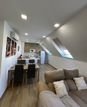 Moderni loft-tyylinen huoneisto, jossa on ruokailutila, keittiö ja viihtyisä oleskelualue, jossa on sohva ja tyynyjä.