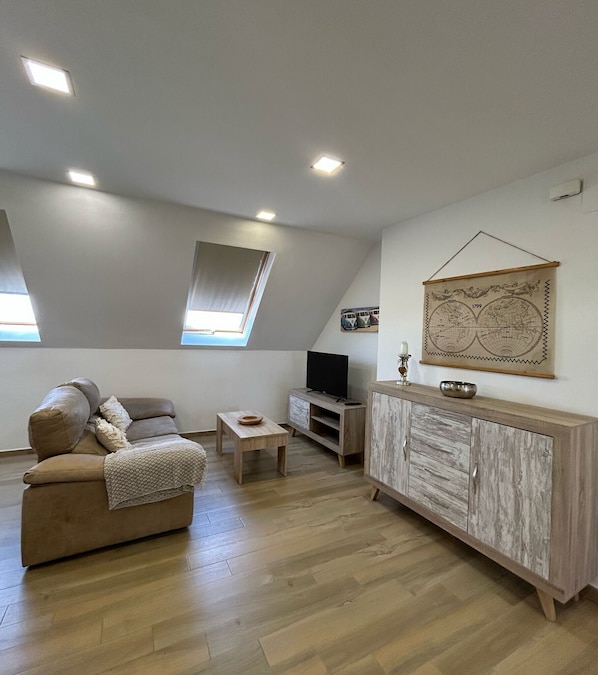 A loft-style room with a sofa, TV, wooden cabinet, and a world map on the wall.