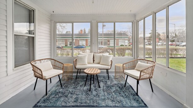 A sunroom with a white ceiling, large windows, a sofa, two wicker chairs, and a small round table. - Boho abode Uptown Maumee by River-GREEN Side! (Maumee)