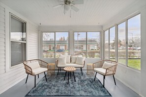 Une véranda avec un plafond blanc, de grandes fenêtres, un canapé, deux fauteuils en osier et une petite table ronde.