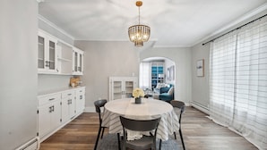 A dining area with a round table, chairs, and a chandelier. There is a white cabinet with glass doors and a blue sofa in the background. - Boho abode Uptown Maumee by River-GREEN Side! (Maumee)
