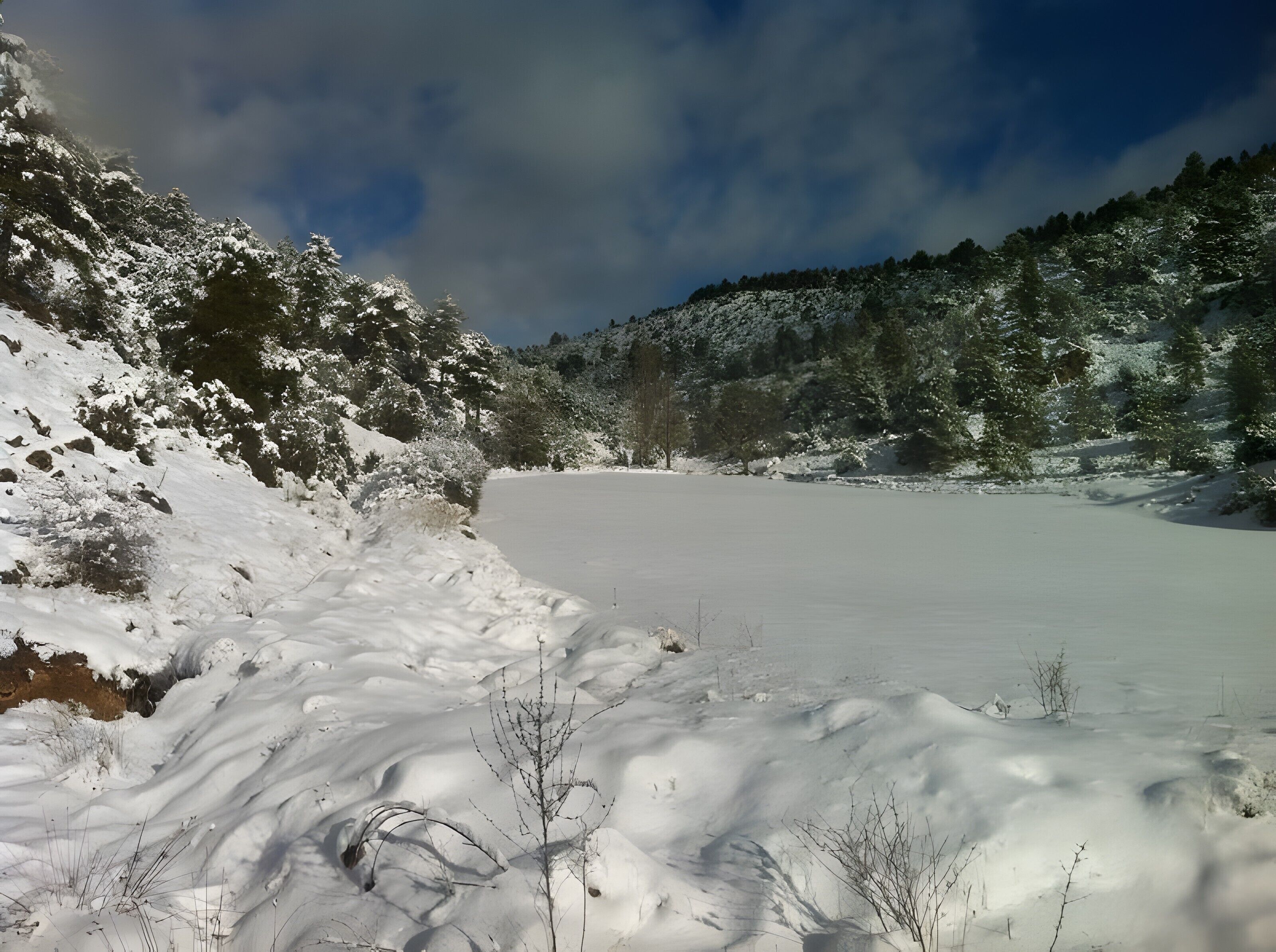 Un paisaje nevado con un lago congelado, árboles y un cielo despejado.