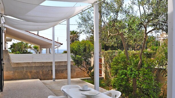 A covered outdoor seating area with a table and chairs, surrounded by greenery and overlooking a scenic view. - Villetta Macao 1 in Torre Suda (Racale)