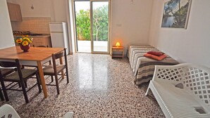 A compact kitchen with a dining table and chairs, a refrigerator, and a window with a view of greenery. - Villetta Macao 1 in Torre Suda (Racale)