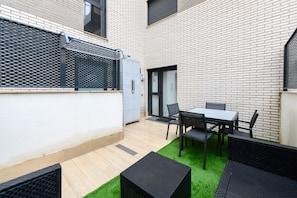 A patio area with a table and chairs, a small black planter, and a grey utility box. - M Alg310b Amplio y Moderno Loft con Terraza Priv (Madrid)