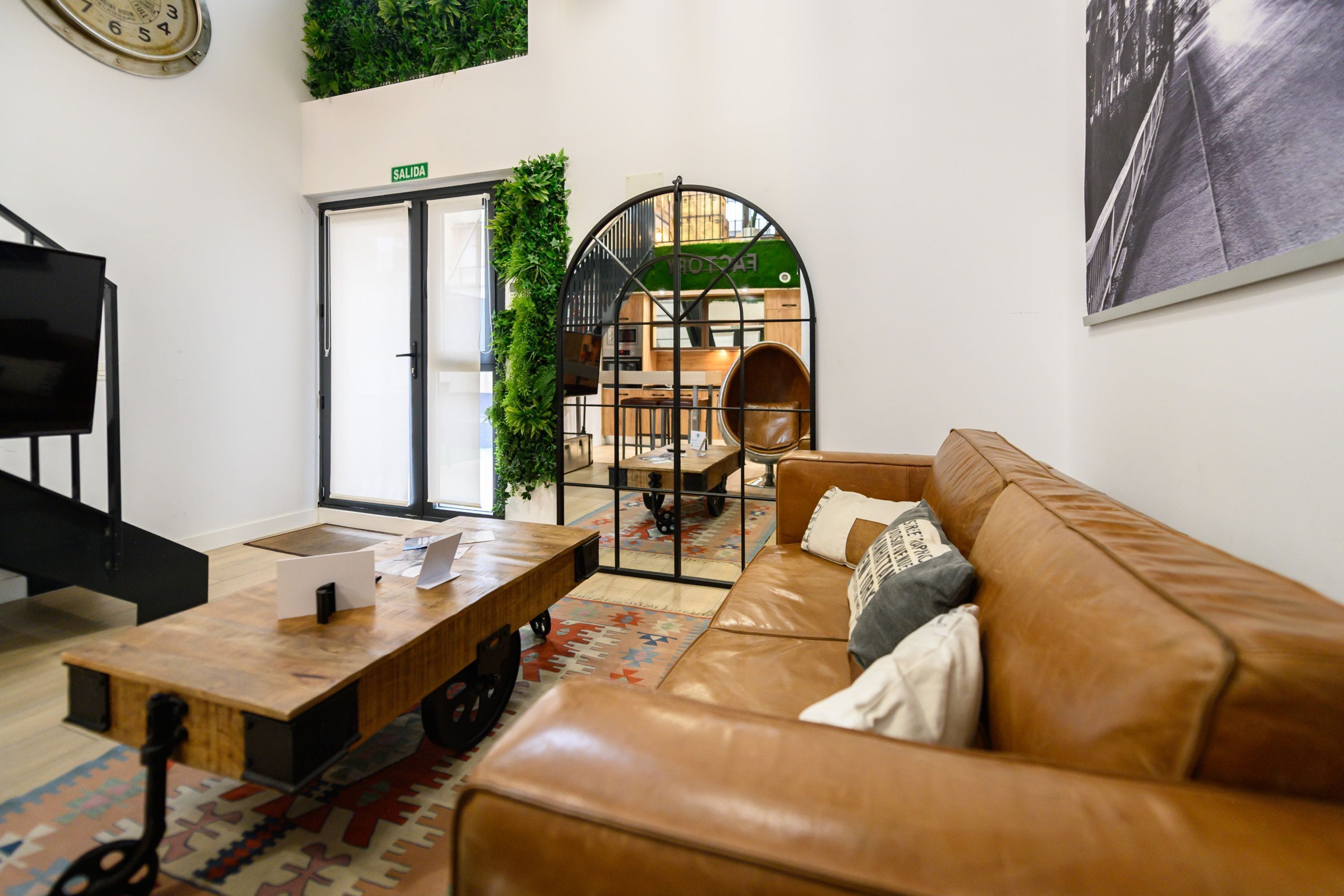 Un interior moderno con un sofá de cuero, una mesa de centro de madera, un televisor y una puerta que indica 'SALIDA'.