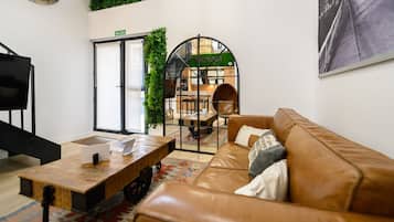 Un interior moderno con un sofá de cuero, una mesa de centro de madera, un televisor y una puerta que indica 'SALIDA'.