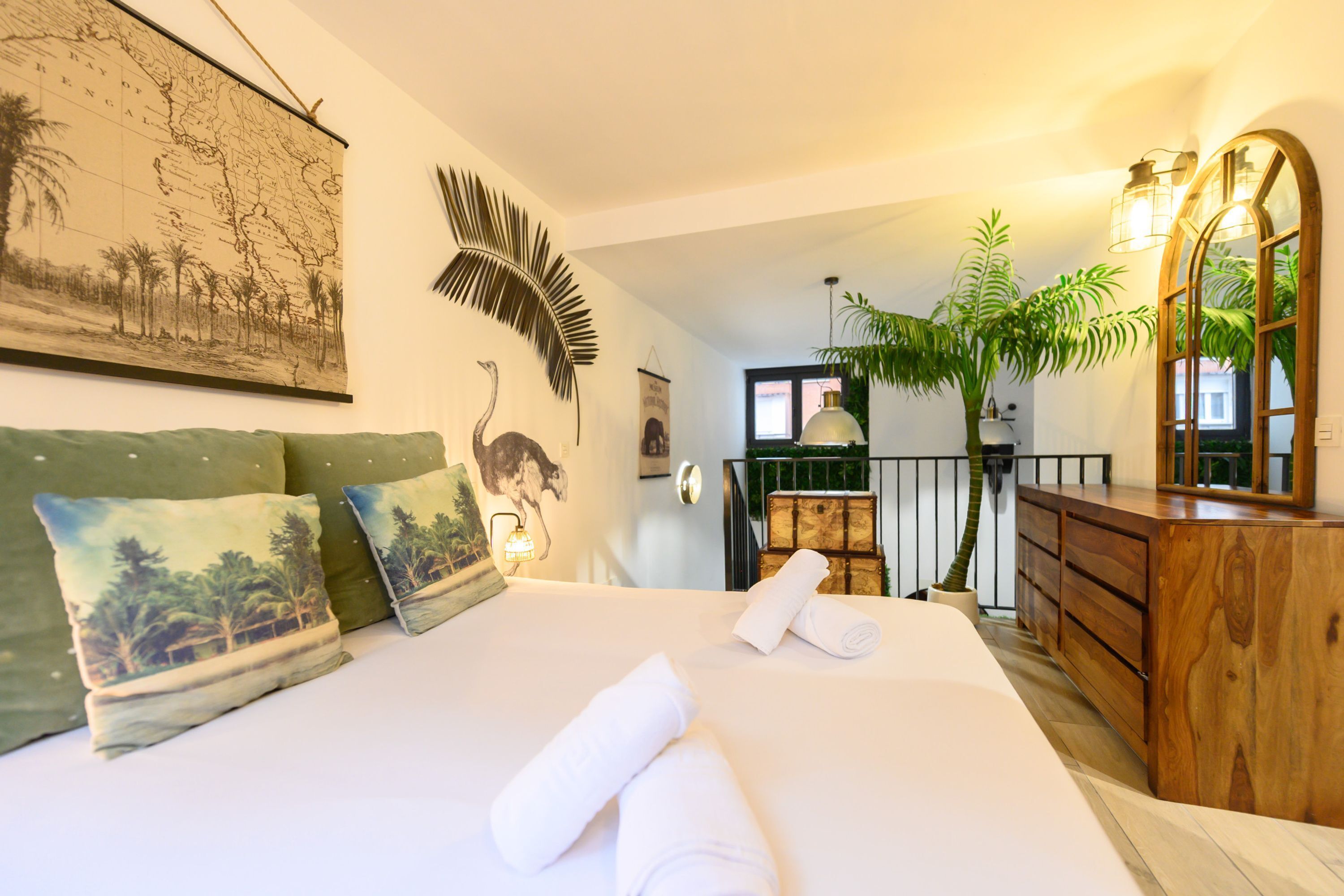 Habitación de hotel con una cama grande, un aparador de madera, un espejo, un mapa en la pared y una planta en maceta.