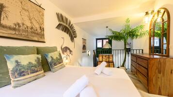Habitación de hotel con una cama grande, un aparador de madera, un espejo, un mapa en la pared y una planta en maceta.