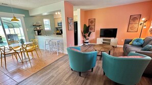 A modern living room with teal armchairs, a wooden dining table, and a kitchen in the background. - Tropical Funky Oasis- near downtown and islands. Pet Friendly! (Savannah)