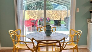 A dining area with a round table and four yellow chairs, a yellow pendant light, and a view of an outdoor patio with red chairs and a wooden fence. - Tropical Funky Oasis- near downtown and islands. Pet Friendly! (Savannah)