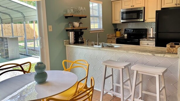 A kitchen with a central island, a dining area with chairs, and a window with blinds. - Tropical Funky Oasis- near downtown and islands. Pet Friendly! (Savannah)