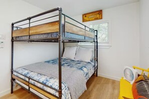 Un lit superposé avec une couvre-lit à rayures, un oreiller blanc et un ventilateur posé sur un pied jaune.