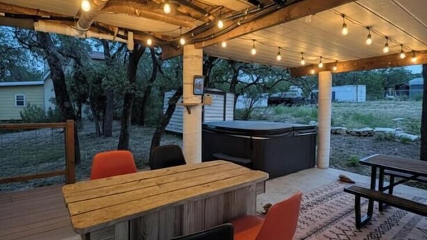 Une terrasse extérieure avec une table et des chaises en bois, un barbecue et des guirlandes lumineuses.