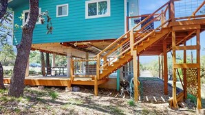 A blue house with a wooden deck and stairs leading to a covered area.