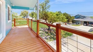 Un terrazza in legno con ringhiera, una vista aperta su una zona residenziale e una casa sullo sfondo.