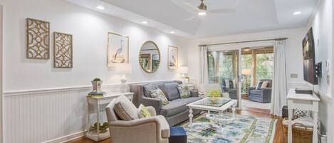 A spacious living room with a grey sofa, a coffee table, and a large window with curtains.