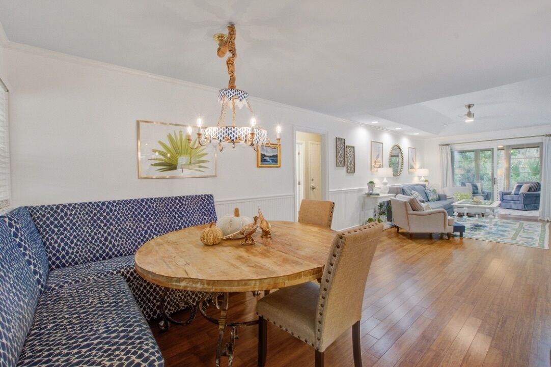 A spacious living room with a round wooden dining table, blue patterned sofa, and a chandelier.