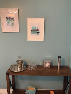 Una mesa de madera con una bandeja, vasos, un termo, un reloj y obras de arte enmarcadas en una pared.
