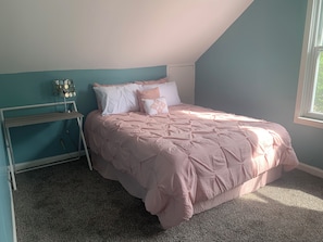 Un dormitorio con cama, mesita de noche, lámpara y ventana.