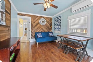 Una habitación con pared de madera en patrón de espiga, sofá azul, mesa de comedor de madera y ventilador de techo.