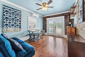 A room with a blue sofa, a ceiling fan, a dining table with benches, and a view through a glass door. - Walk to Lake! Budget Friendly Views & Hot/Cold Tub (Canyon Lake)