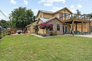 A two-story house with a covered porch, a stone facade, and a small garden with pink flowers. - Walk to Lake! Budget Friendly Views & Hot/Cold Tub (Canyon Lake)