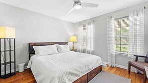 Un dormitorio con cama, lámpara de pie, ventilador de techo y ventana con cortinas.