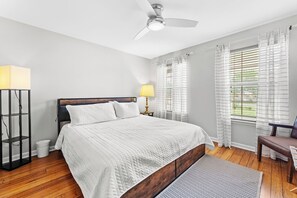 Ein Schlafzimmer mit einem Bett, einer Stehlampe, einem Deckenventilator und einem Fenster mit Vorhängen.